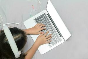 menina deitado e vestindo fones de ouvido para aprender conectados a partir de uma computador portátil foto