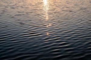 o sol brilhando na água ondulada do lago pela manhã foto