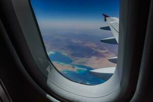 Visão através a janela a partir de a avião durante uma voar sobre a deserto com a vermelho mar foto