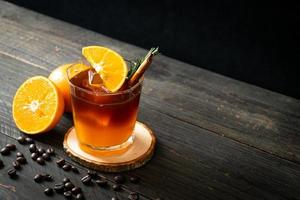 um copo de café preto americano gelado e uma camada de suco de laranja e limão decorado com alecrim e canela foto