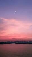 vertical imagem, crescente lua dentro dramático vibrante cor céu com silhueta panorama do montanhas e lago, crepúsculo, natureza papel de parede fundo foto