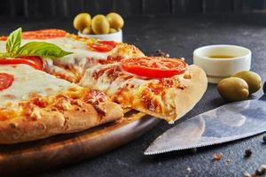 pizza talian e ingredientes para cozinhar em um fundo de concreto preto tomates azeitonas manjericão e especiarias foto