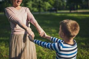 feliz mãe é jogando com dela filho dentro parque. elas estão segurando mãos. foto