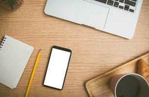 topo Visão do Móvel inteligente telefone Preto branco zombar acima em branco cópia de espaço para usar. em escrivaninha com computador portátil e café croissant, caderno e lápis em de madeira mesa foto