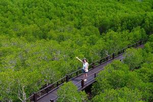 vista de cima de uma jovem asiática caminhando em uma trilha de madeira em uma floresta de mangue durante as férias de verão foto