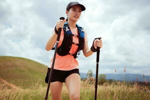 trilha ativa de mulheres jovens atravessando um prado em uma trilha gramada no alto das montanhas à tarde com vara de trekking foto