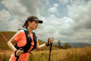 trilha ativa de mulheres jovens atravessando um prado em uma trilha gramada no alto das montanhas à tarde com vara de trekking foto