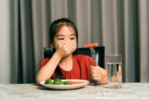 pequeno fofa criança menina recusando para comer saudável legumes. crianças Faz não gostar para comer legumes. foto