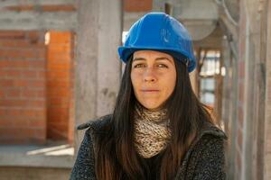 retrato do a engenheiro em uma construção local olhando às a Câmera. fêmea construção local Gerente dentro azul Difícil chapéu. foto