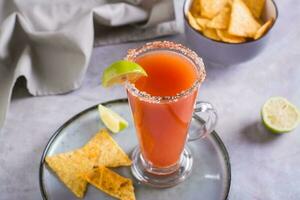 Michelagua mocktail com tomate suco e Lima suco dentro uma vidro e nachos dentro uma tigela foto