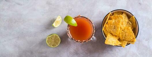 Michelagua mocktail com tomate suco e Lima suco dentro uma vidro e nachos topo Visão rede bandeira foto