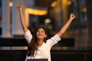 jovem mulher asiática com rosto feliz e surpreso usando laptop em uma cidade foto