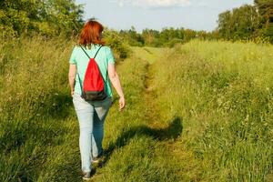 uma menina com uma mochila anda em ao longo uma país estrada em uma verão dia, caminhada foto