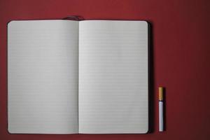 cigarro e caderno escrevendo sobre um fundo vermelho foto