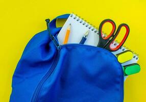escola mochila, lápis, caneta, marcadores, tesouras e bloco de anotações em uma amarelo fundo. foto