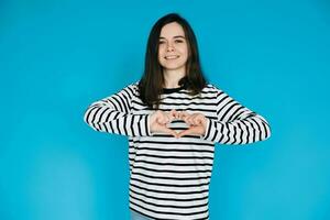 alegre mulher dentro listrado suéter sorridente, gesticulando coração mãos - símbolo do amor e felicidade - isolado em azul fundo - perfeito para positivo emoções, amor, e estilo de vida conceitos foto