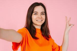 uma vivazmente deslumbrante menina com uma radiante sorriso, com confiança mostrando a v placa com dela dedos. em uma Rosa fundo. em branco espaço para adicionar texto ou gráficos para festa, feriado e promocional Projeto foto