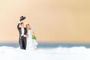 pessoas em miniatura, casal de noivos feliz em uma praia branca, conceito de casamento foto