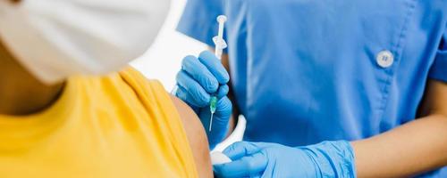 Feche a mão da médica segurando a seringa e usando algodão antes de fazer a injeção no paciente na máscara médica. vacina covid-19 ou coronavírus foto