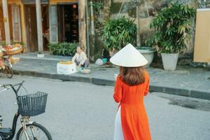 feliz mulher vestindo ao dai vietnamita vestir, ásia viajante passeios turísticos às Hoi a antigo Cidade dentro central Vietnã. ponto de referência e popular para turista atrações. Vietnã e sudeste viagem conceito foto
