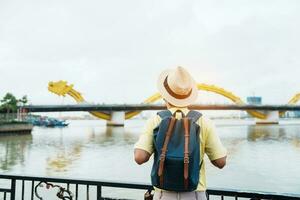 homem viajante com mochila visitando dentro da nang. turista passeios turísticos a rio Visão com Dragão ponte às amor trava ponte. ponto de referência e popular. Vietnã e sudeste Ásia viagem conceito foto