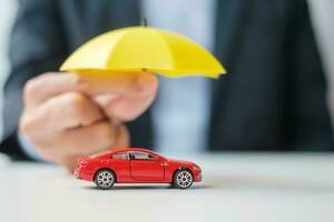 mão de empresário segurando o guarda-chuva e cobrir o brinquedo do carro vermelho na mesa. seguro de carro, garantia, reparo, financeiro, bancário e conceito de dinheiro foto