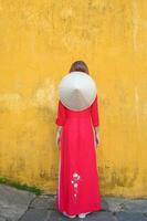 feliz mulher vestindo ao dai vietnamita vestir e chapéu, viajante passeios turísticos às Hoi a antigo Cidade dentro central Vietnã. ponto de referência e popular para turista atrações. Vietnã e sudeste viagem conceito foto