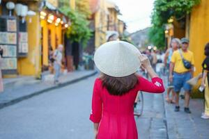 feliz mulher vestindo ao dai vietnamita vestir, ásia viajante passeios turísticos às Hoi a antigo Cidade dentro central Vietnã. ponto de referência e popular para turista atrações. Vietnã e sudeste viagem conceito foto