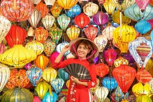 feliz mulher vestindo ao dai vietnamita vestir com colorida lanternas, viajante passeios turísticos às Hoi a antigo Cidade dentro central vietnam.landmark para turista atrações.vietnam e sudeste viagem conceito foto