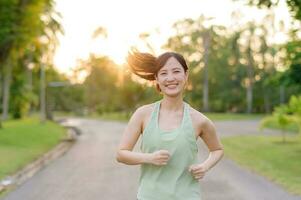 em forma ásia jovem mulher corrida dentro parque sorridente feliz corrida e desfrutando uma saudável ao ar livre estilo de vida. fêmea corredor. ginástica corredor menina dentro público parque. saudável estilo de vida e bem estar ser conceito foto