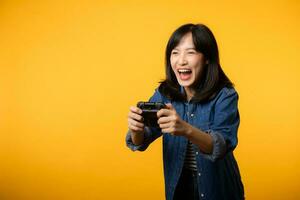 retrato jovem ásia mulher com feliz sucesso sorrir vestindo jeans roupas segurando controle de video game controlador e jogando vídeo jogo. Diversão e relaxar passatempo entretenimento estilo de vida conceito. foto