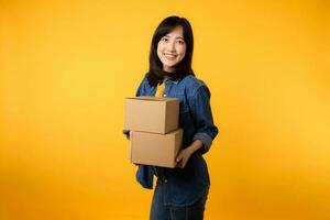 retrato ásia jovem mulher vestindo amarelo camiseta e jeans camisa segurando parcela caixa isolado em amarelo estúdio fundo, Entrega correio e Remessa serviço conceito. foto