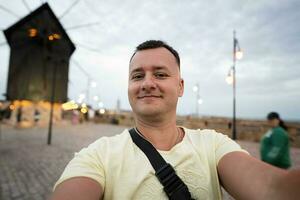 retrato do uma sorridente turista homem levando selfie em a passeio perto moinho do nessebar, Bulgária. foto