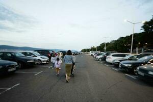 mãe com crianças caminhando dentro a estacionamento muitos dentro a cidade às crepúsculo. foto