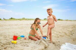 crianças jogar com areia em de praia. menina rompe castelo do areia, namorada gritos. foto