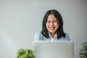 jovem sorridente ásia o negócio mulher empregado trabalhando em computador portátil dentro corporativo escritório. feliz profissional empresária marketing Gerente usando computador tecnologia foto