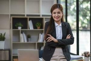 lindo ásia empresária ficar de pé às escritório mesa, sorridente e olhando às Câmera. foto