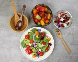 lindo colorida amarelo tolet wite vermelho comestível flores em ganância jardim salada tomate mármore mesa topo tigela de madeira colher em branco fundo cópia de texto espaço foto