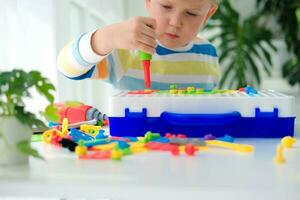 pequeno Garoto jogando conjunto com uma Chave de fenda e uma furar, e parafusos e partes . a criança tocam construtor com uma brinquedo broca para desenvolve imaginação e motor habilidades. educacional lógica brinquedos para crianças. foto