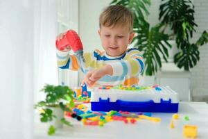 pequeno Garoto jogando conjunto com uma Chave de fenda e uma furar, e parafusos e partes . a criança tocam construtor com uma brinquedo broca para desenvolve imaginação e motor habilidades. educacional lógica brinquedos para crianças. foto