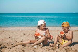 retrato do crianças do irmã e irmão em a de praia com Melancia. menina e pequeno Garoto estão comendo em a de praia. a crianças teve uma piquenique de a mar. cópia de espaço. foto