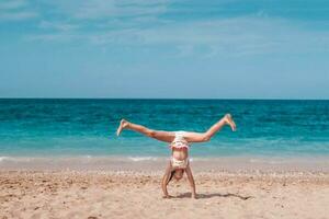 a menina faz uma ginástica roda elemento em a fundo do a mar. a criança é em repouso em a de praia dentro verão. verão tempo. viagem. foto