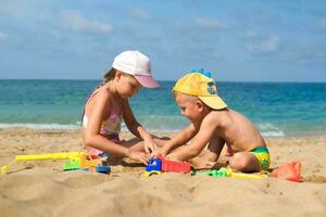 irmão e irmã jogar em a de praia com plástico brinquedos com areia.crianças estão jogando em a de praia. verão água Diversão para a todo família. uma Garoto e uma menina estão jogando com areia em a Beira Mar. foto