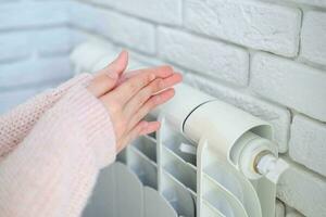 a criança é mãos caloroso seus mãos perto a aquecimento radiador. salvando gás dentro a aquecimento temporada. foto