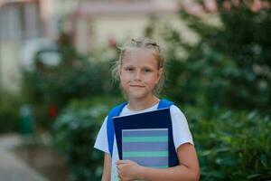 retrato do uma menina com uma pasta e cadernos dentro dela mãos em a rua. costas para escola. foto