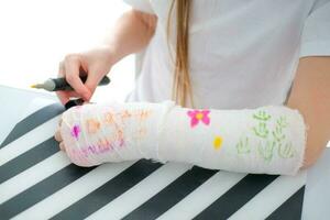 uma pequeno menina tintas uma fundida em dela braço. uma criança desenha uma desenhando em uma fundida depois de uma mão ferida. foto