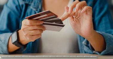 jovem asiática usando computador pede um produto de compras online e paga a conta com cartão de crédito no interior da sala de estar foto