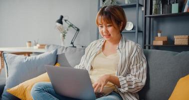 roupa casual para senhora freelance asiática usando laptop aprendizagem on-line na sala de estar foto