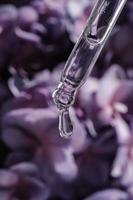 uma solta do Cosmético óleo cai a partir de a pipeta em uma roxa floral fundo. foto