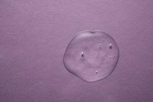 uma gotas do transparente Cosmético gel em uma roxa fundo. foto